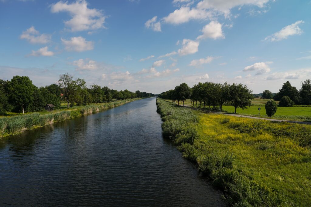 Vacatures bij de gemeente: kanaal met bomen en weilanden onder een blauwe lucht