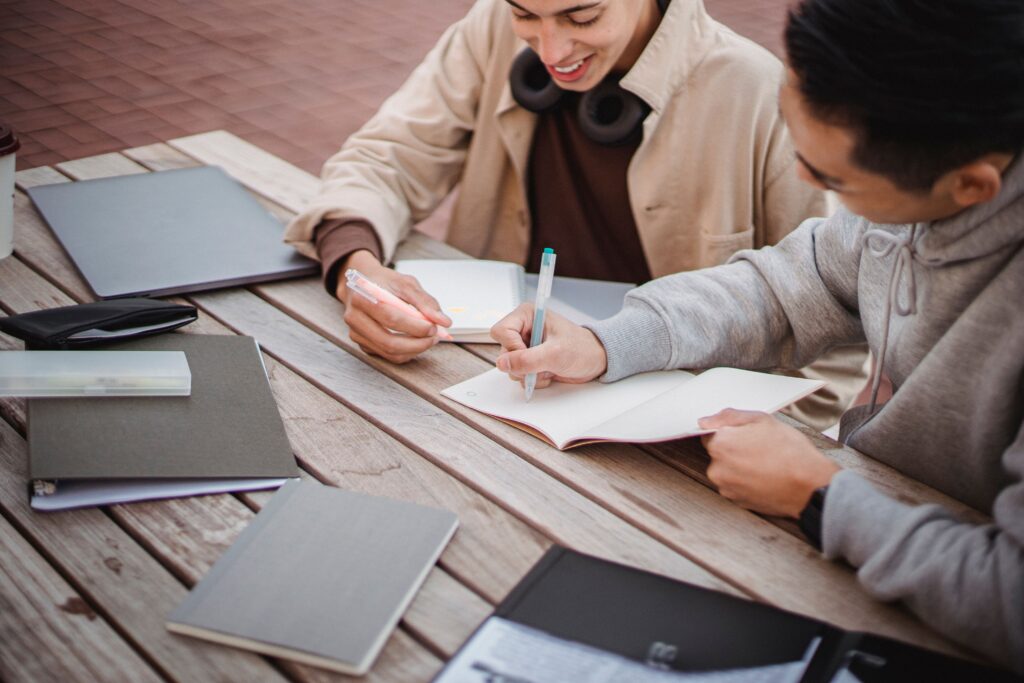 Vacatures in het onderwijs: twee studenten studeren samen buiten op de campus met boeken laptops